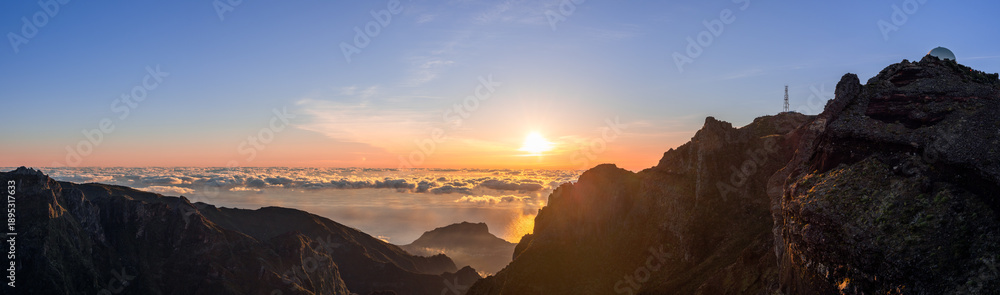 Fototapeta premium Ultra wide sunrise panorama from Pico do Arieiro Madeira Portugal high ridge, bright dawn lights sea of clouds above Atlantic cliffs valleys and distant island silhouettes seen from famous viewpoint