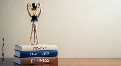 Achieving Business Success: Wooden Mannequin Holding Trophy Atop Books Representing Strategy, Leadership and General Business Acumen