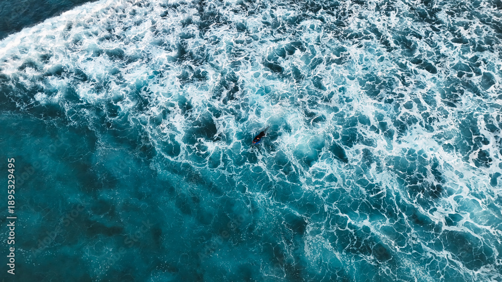 Fototapeta premium Surfer Swimming Amid White Ocean Foam in Deep Blue Sea