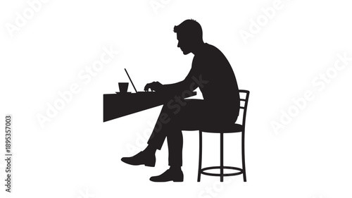 A man sitting on a stool working on a laptop at a desk with a cup and straw in a professional setting profile view