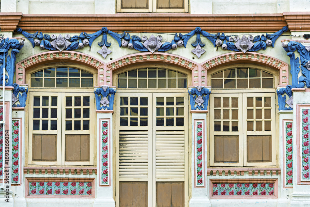 Fototapeta premium decorated facade along Jalan Besar Road, Singapore, known for its eclectic architectural heritage. The design features three large blue-framed windows with white panes, each crowned by sculpted arches