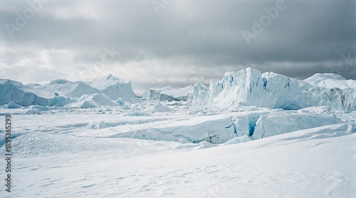 Vast glacial landscape stretches toward towering blue ice formations beneath a heavily clouded and dramatic polar sky creating a scene of extreme cold.