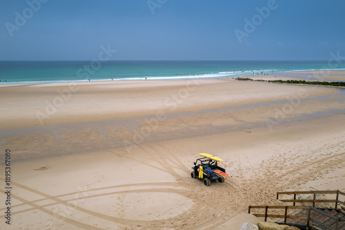 Lifeguard vehicle on sandy beach with surfers in the Atlantic Ocean, Lacanau, France