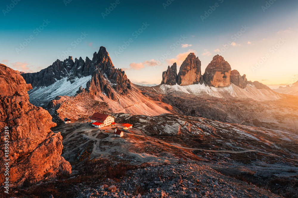 Fototapeta premium Alpine landscape of sunset over Tre Cime mountain peak and mountain hut during autumn in Dolomites, Italy