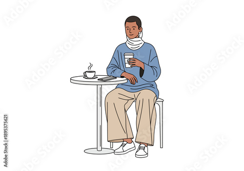Person sitting at a small round table holding a beverage and looking at a device with a hot drink in a cup on the table and a mobile phone nearby