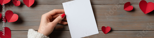 Woman's hand holding blank vertical card for Valentine's Day. Woman's hand holding white blank greeting card mockup with scattered red hearts
