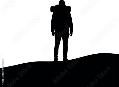 Silhouette of a hiker with a backpack standing on a hilltop at sunset