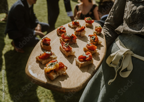 Close up of a tray of wooden tray of canapes with mini bruschetta being served at a gaden party or wedding