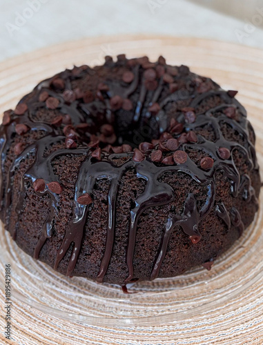 Rich chocolate bundt cake with drizzled ganache and chips on woven placemat - concept of bakery, cafe, catering