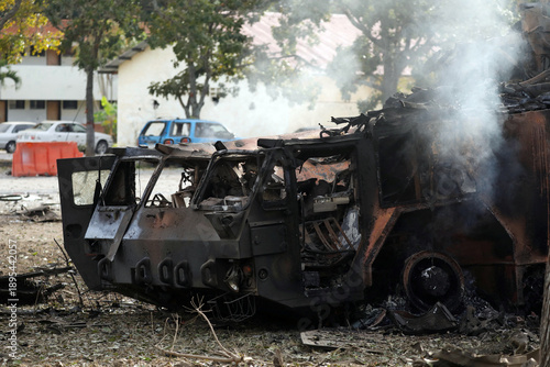 Burnt Out Military Vehicle in Conflict Zone with Smoke and Debris