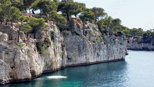 Cassis, France - 14 July 2025: Young people jumping from the cliff into the water at Port Miou calanque in the Calanques National Park, captured from the sea.