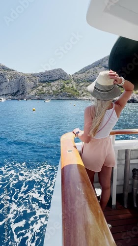 Young woman in a hat on a boat ride in Calanque de Morgiou bay, turquoise Mediterranean water and limestone cliffs in Calanques National Park, French Riviera, France.