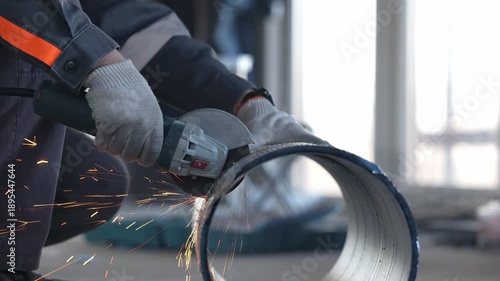 A worker cuts a ventilation pipe with an angle grinder