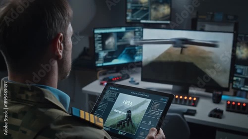 A military personnel in camouflage clothing holds a tablet with a drone image, surrounded by multiple computer monitors displaying aerial views and controls