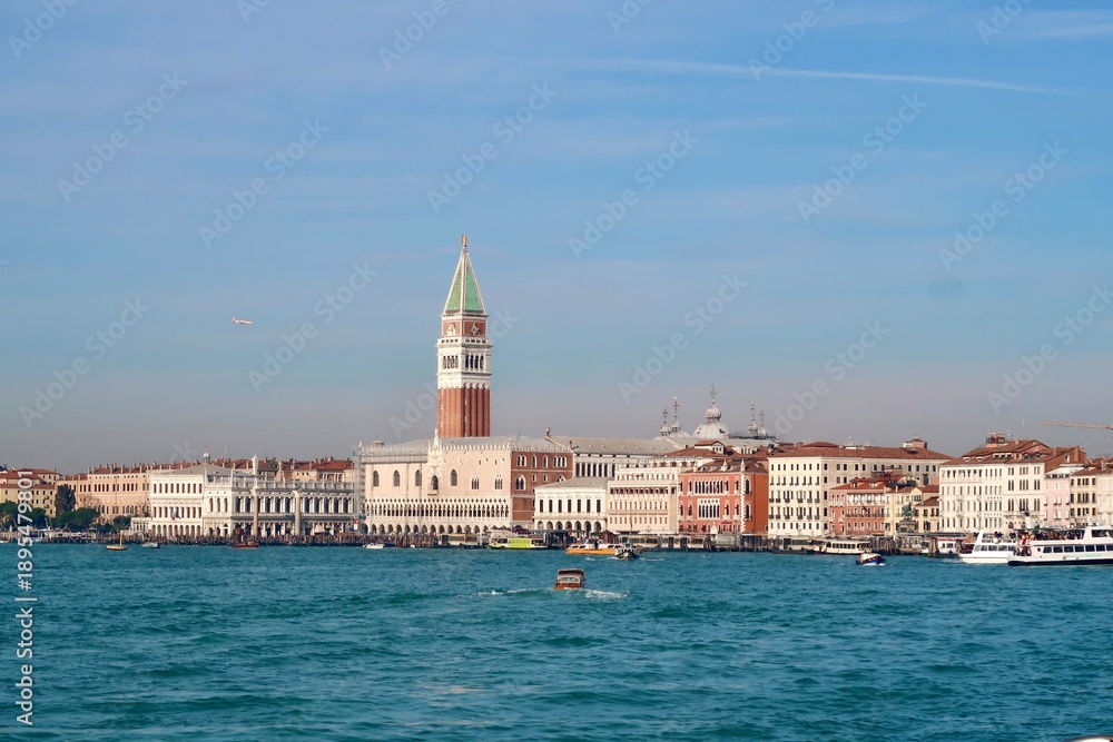 Obraz premium Venice Skyline with St Mark’s Campanile and Grand Canal - Panoramic view of Venice skyline with St Mark’s Campanile, historic buildings, and boats on the water under a clear blue sky in Italy. 