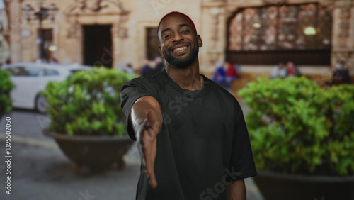 Schilderij op canvas Man offers outstretched hand for handshake on a city street in front of building, smiling and leaning forward; friendly greeting