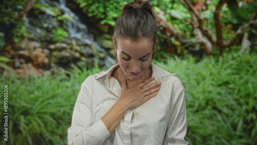 Photos Young hispanic woman clutch chest in lush green forest under soft sunlight with gentle breeze rustling leaves; serenity