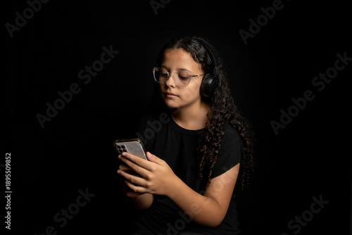 Brazilian teenager, a beautiful young Brazilian girl with a cell phone and headphones, low key, black background, selective focus.