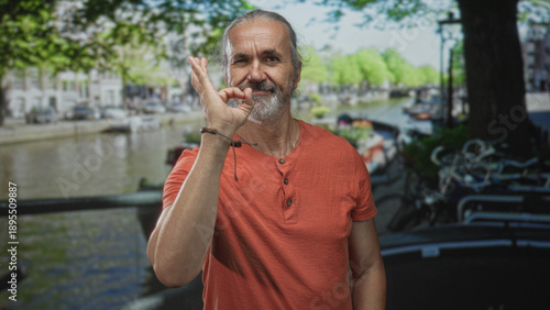 Canvas Print Middle age man giving thumbs up with hand on an amsterdam canal street by water and bicycles; optimism