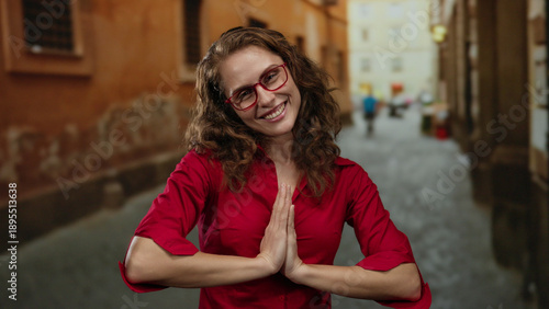 Wallpaper Mural Woman smiling with hands in prayer position on a city street wearing a red shirt and glasses with a joyful expression amidst urban background. Torontodigital.ca