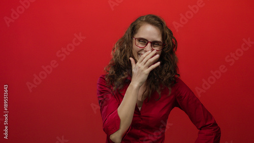 Woman laughing in front of a vibrant red wall dressed in a red shirt and glasses, capturing a candid joyful moment in a studio setting.