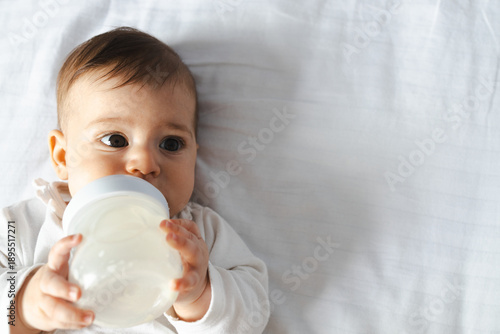 Fotografía Cute Baby Drinking Milk from Bottle on White Bedding