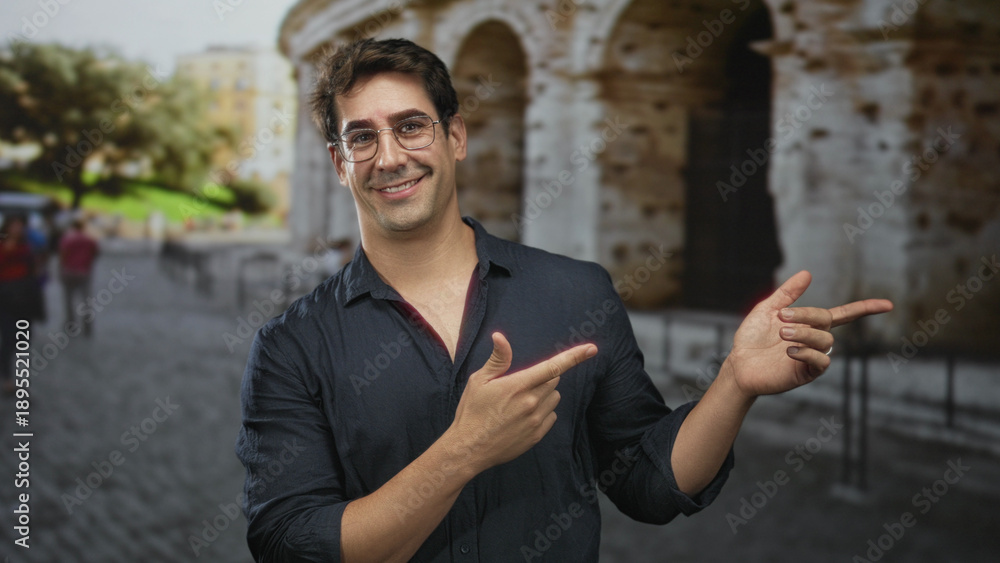 Fototapeta premium Man pointing with fingers and smiling in front of historic building on a street; playful confidence.