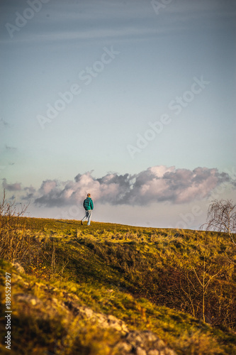 Lone person walking on a grassy hill under expressive cloudy sky