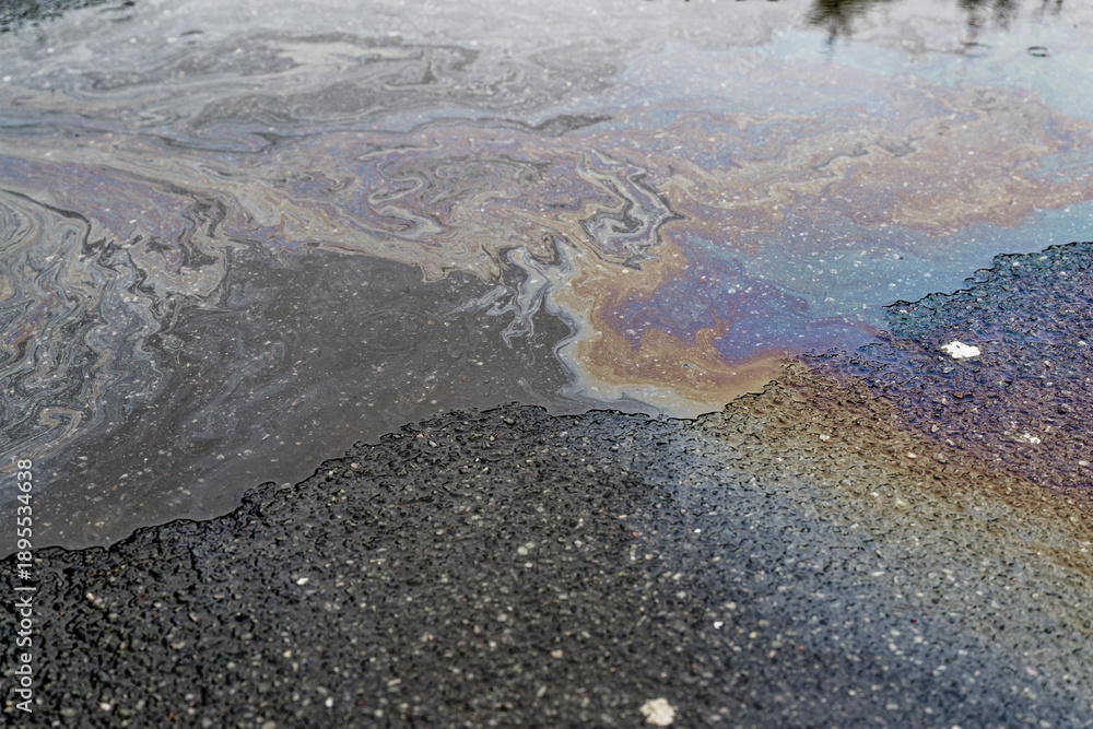 Fototapeta premium Iridescent oil and fuel streaks across puddle on asphalt.