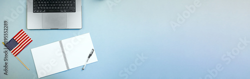 national banner with tech devices, stars and stripes alongside electronic gadgets on workspace table, american flag displayed near laptop and journal on vibrant blue desk for planning