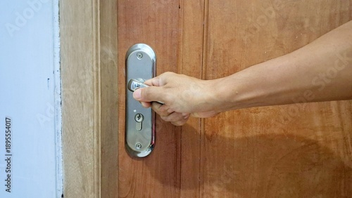 Hand opening silver door handle close up view on brown wooden door background concept of opportunity privacy safety and entrance to a room professional stock photo high resolution detail