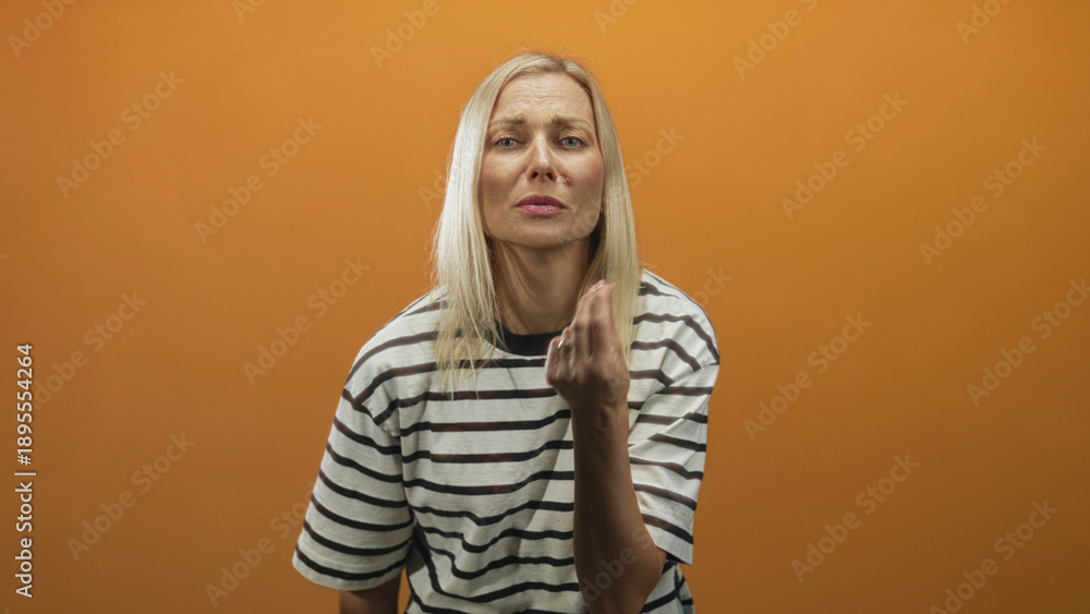 Fototapeta premium Woman beckons with fingers toward camera and later visibly rubs forehead in orange studio; plea frustration.