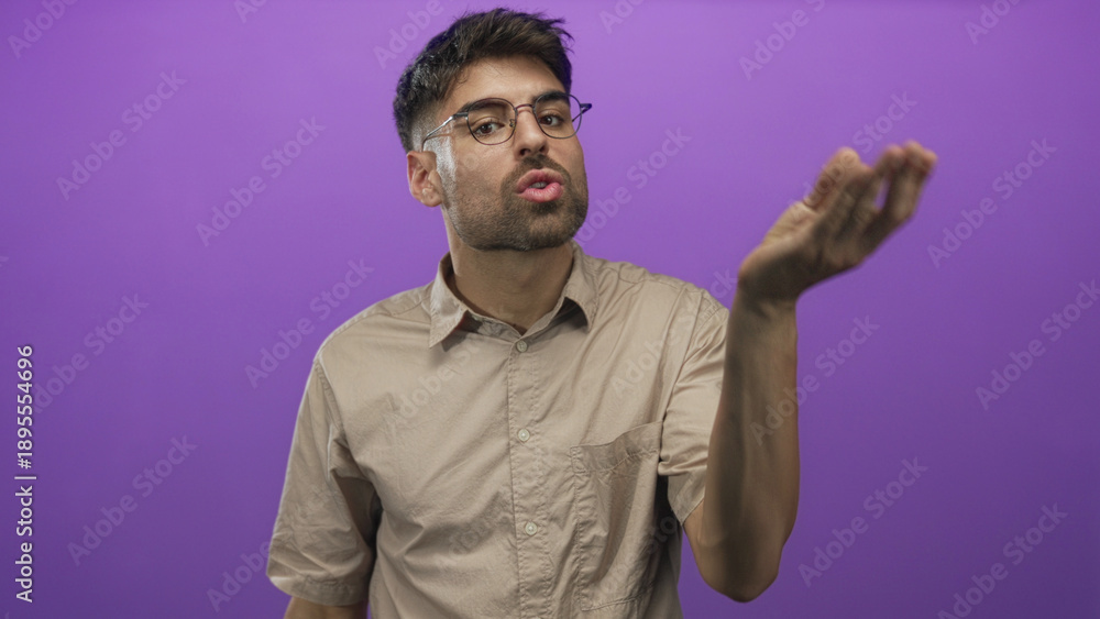 Naklejka premium Hispanic man wearing glasses and beige shirt blowing kiss gesture with lips in purple studio; affection tenderness.