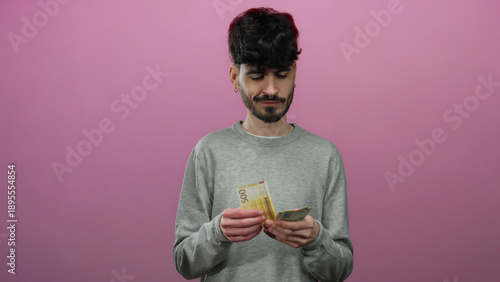 Man holding norwegian krone banknotes smiling against isolated pink background expressing financial happiness and prosperity with a casual look.