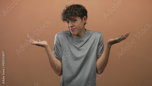 Cuadro en lienzo Teenage boy in gray tshirt shrugs with bare hands, palms up and smirks, showing necklace against a studio backdrop; casual uncertainty