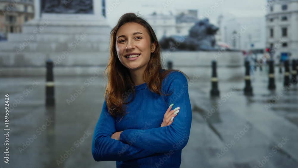 Fototapeta premium Woman smiling and crossing arms in a vibrant city street with historic architecture and iconic structures suggests a positive urban experience outdoors.