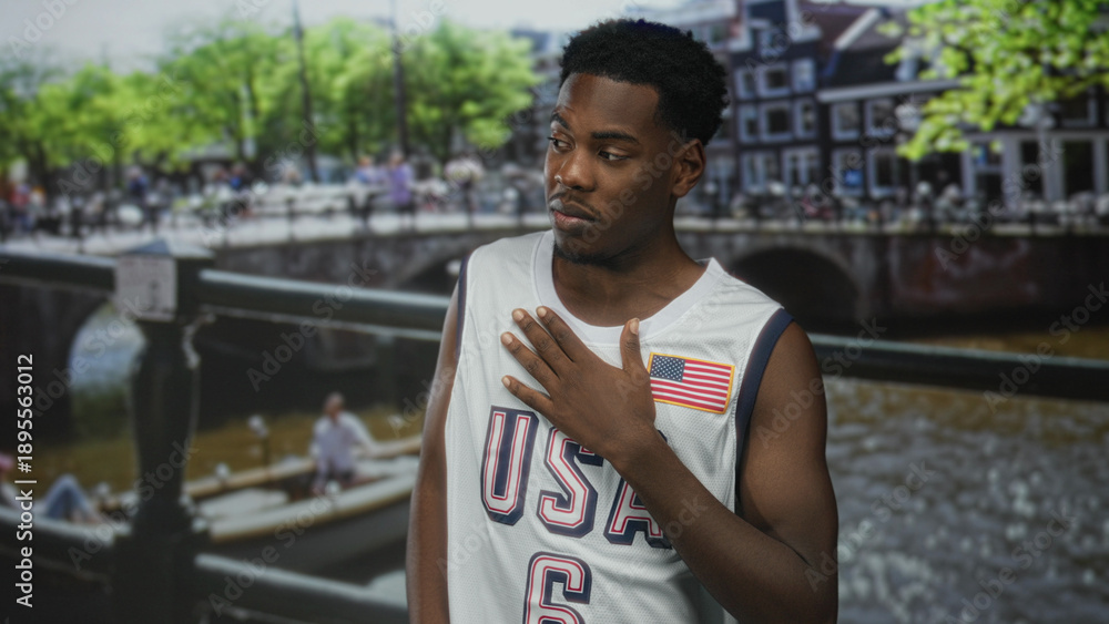 Fototapeta premium Young african american man in white sleeveless jersey clutch chest for heartattack on canal by railing; distress.