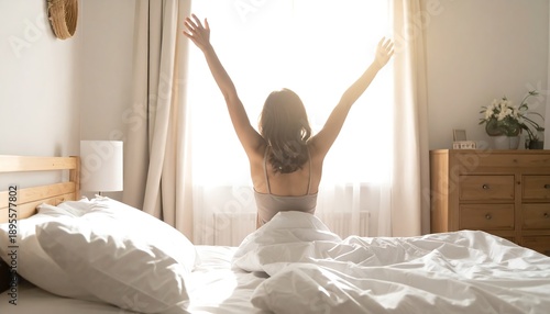 Back view of woman stretching on bed facing window filled with warm sunlight creating peaceful morning mood