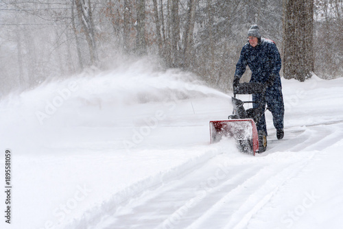 Bilde på lerret A front view of a man wearing winter coveralls using a snow blower to clear the