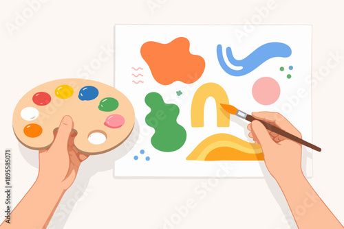 Artist hands holding palette and paintbrush creating abstract shapes on canvas
