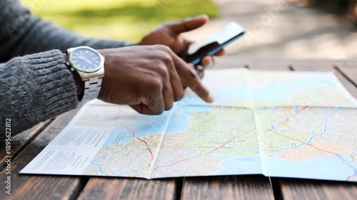 Person planning trip with map and smartphone on wooden table outdoors
