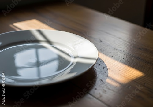 Plain white plate sitting on a wooden table in a shaft of sunlight