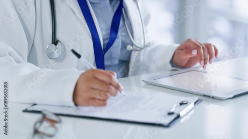 Doctor, tablet and writing prescription or report with online research or consultation on a mobile app while sitting at desk, Professional female GP and healthcare worker with medical insurance form