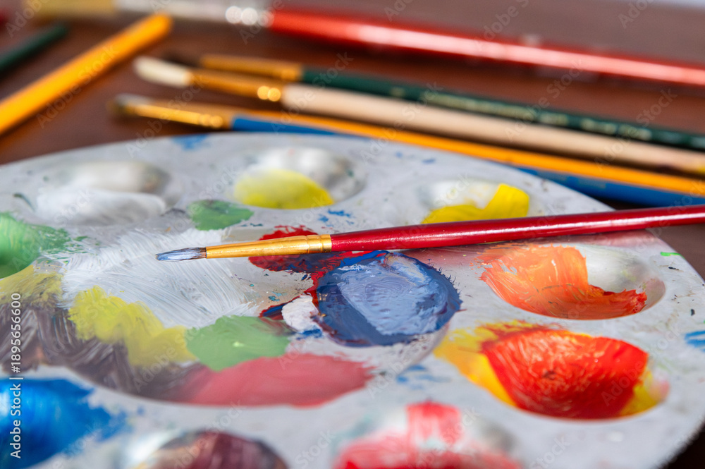 Fototapeta premium A paint brush sitting on top of a paint pallette filled with colorful paint