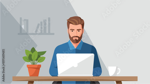 A bearded man in a blue shirt working on a laptop at a wooden desk with a plant and coffee cup.