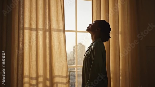 A moment of tranquil awakening as a woman stands by a sunlit window, embracing the peaceful start of a new day
