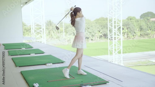 Golf instructor teaching swing technique to Asian woman at driving range