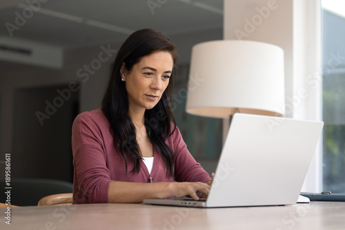 Focused middle-aged Latin woman working on laptop at homeoffice room, chatting, responding on business e-mails, learning received notification, answers on messages by personal or work-related matters