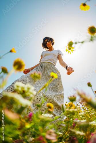 Summer mood. a young and cheerful girl posing against a background of blue sky and flowers. A beautiful girl dances among flowers. Happy girl among blooming flowers, outdoors.