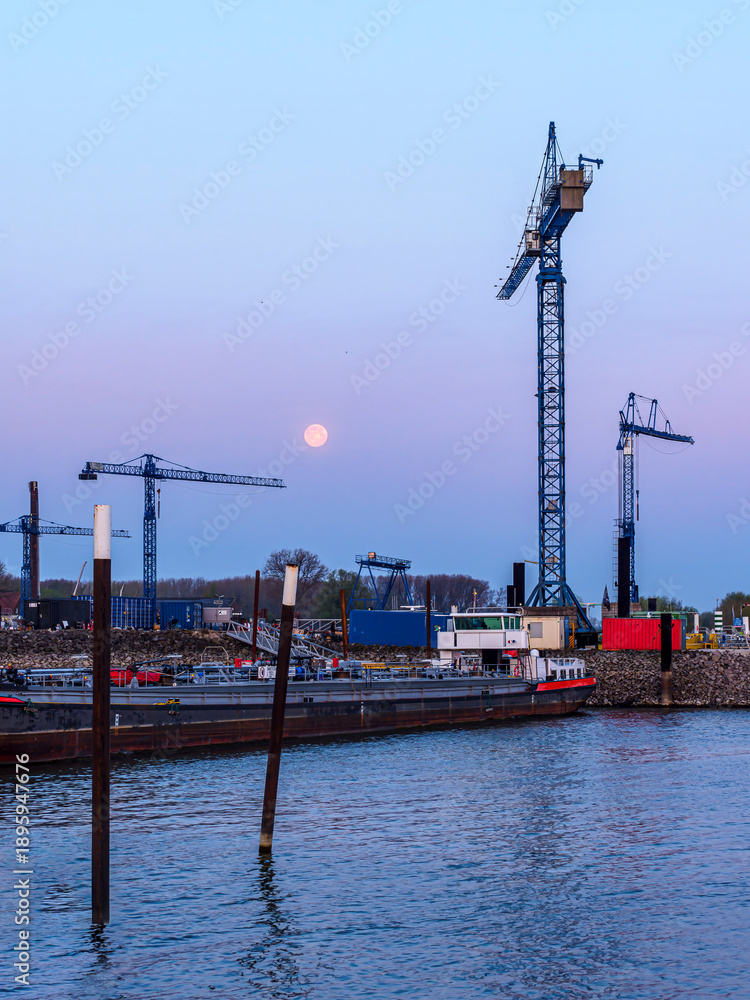 Obraz premium Cranes and full moon over industrial harbor at dusk